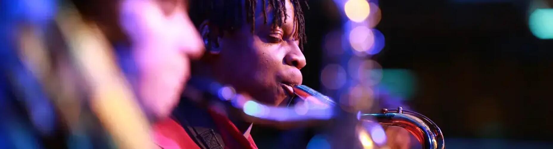 Young person on stage playing the saxophone as part of an orchestra.