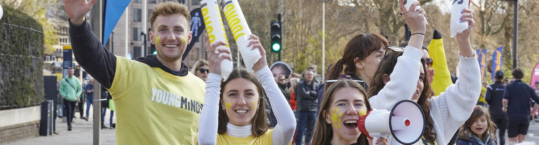 Three young people in yellow YoungMinds stand outdoors at a demo smiling and facing the camera - one holds a megaphone