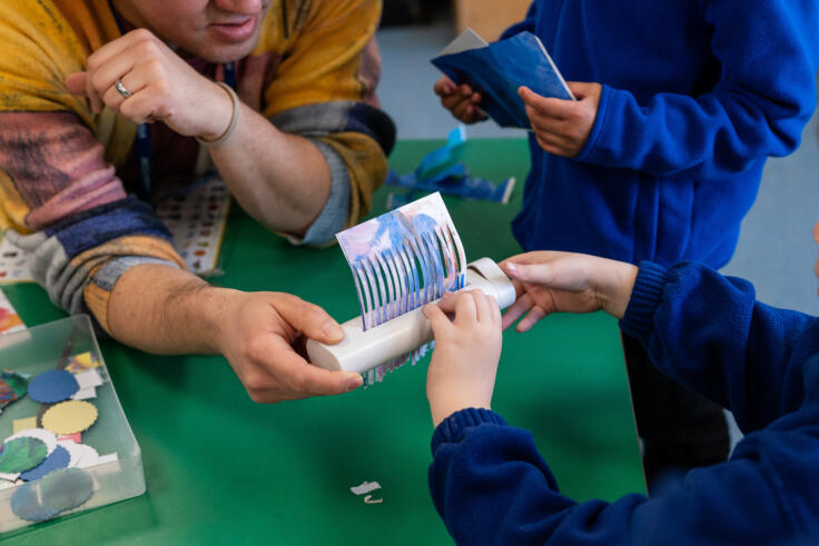 Artist supporting children in school to shred colourful paper for visual arts activity.