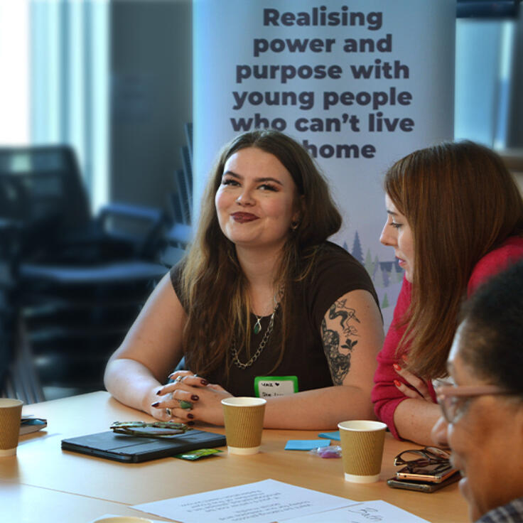 Young person sitting in front of a banner that reads ‘realising power and purpose with young people who can’t live at home’