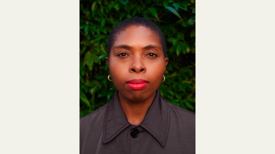 Artist stands and looks to the side against a green, leafy background