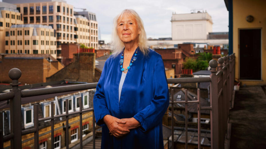 Artist stands in a silky royal blue dress on a balcony with an urban landscape in the background