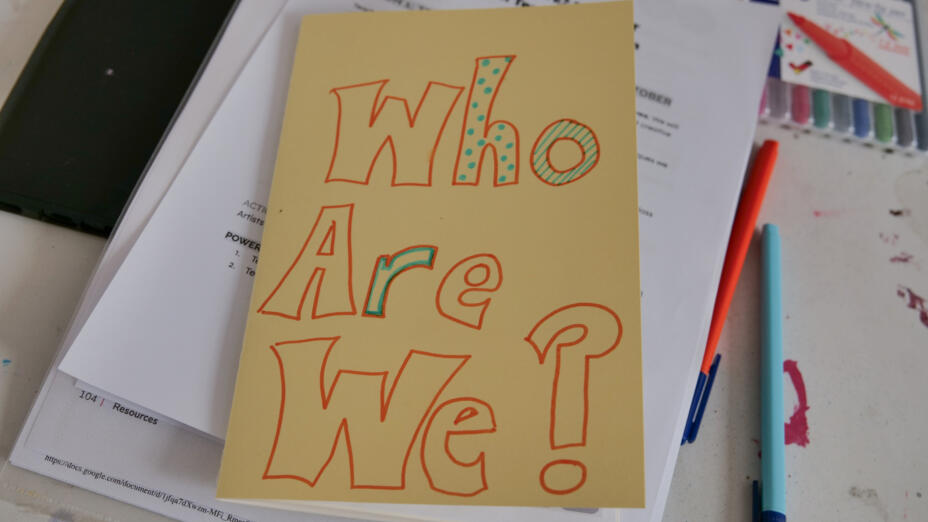 Yellow card with the words 'who are we?' written in red marker