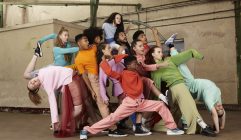 A group of young people from Jukebox Collective are frozen in dynamic poses, wearing an array of bright colours